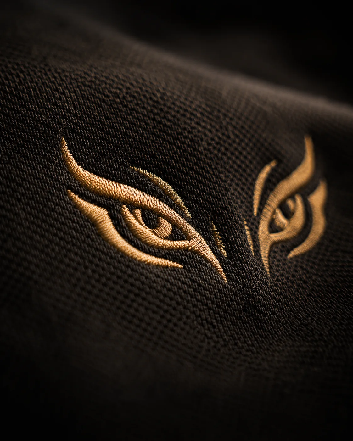Gold tiger eyes embroidery detail on Panthera Prowl polo — 280 GSM organic cotton